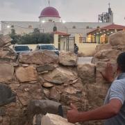 A man looks through a gap in a stone wall toward a Greek Orthodox church where gunmen opened fire during a funeral hours earlier in Hamoud village, in Jordan’s Karak governorate (AP)